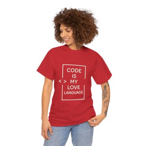 May include: A red t-shirt with the text "CODE IS MY LOVE LANGUAGE" in a white rectangular box. The shirt has short sleeves and a crew neck. The model is wearing blue jeans.