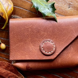 May include: A brown leather wallet with a stitched circle detail. The wallet has a flap that folds over the front.