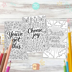 May include: Three adult coloring book pages with floral and butterfly designs. The pages have the phrases "You've got this", "Choose joy", and "Create your own sunshine". Colored pencils are scattered around the pages.