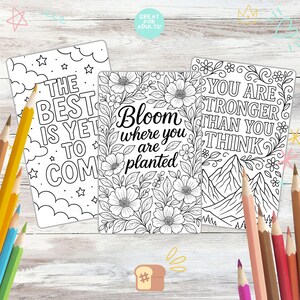 May include: Three black and white coloring pages with inspirational quotes and floral designs. The pages include the phrases "The Best Is Yet To Come", "Bloom where you are planted", and "You are stronger than you think". Colored pencils are scattered around the pages.