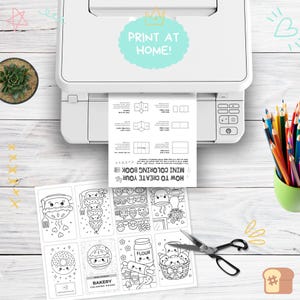 May include: A white printer printing a black and white mini coloring book page. The page features instructions and bakery-themed coloring pages. A pair of scissors and a pot of colored pencils are also visible.