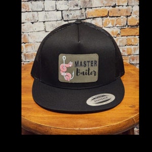 May include: Black trucker hat with a green patch that says "Master Baiter" with a cartoon worm on a hook. The hat has a black mesh back and a black snap closure.