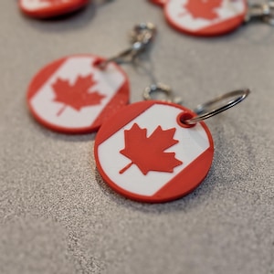 May include: A set of four keychains featuring a red maple leaf on a white background, representing the Canadian flag. The keychains are made of red and white plastic and have a silver metal ring.
