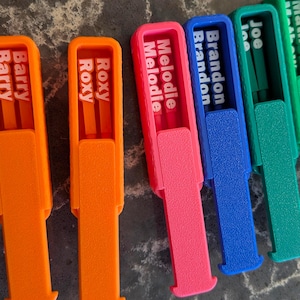 May include: A selection of brightly coloured name tags, including orange, pink, blue, and green. Each tag displays a different name in white lettering: "Barry", "Roxy", "Melodie", "Brandon", "Joe", and "Mathew".