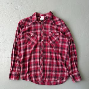 May include: A red and black plaid long-sleeve shirt with two chest pockets and white buttons. The shirt has a classic western style with a collared neckline and is made of a soft, woven fabric.