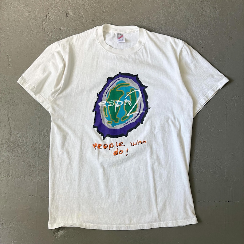May include: A white short-sleeve t-shirt featuring a central graphic of a stylised globe in green, blue, and purple. The text "esprit" is written in white across the globe, with the orange text "people who do!" printed directly below the graphic.