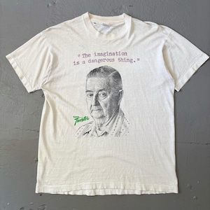 May include: A white short-sleeve t-shirt featuring a black and white sketch of an older person. Above the portrait, the text reads, "The imagination is a dangerous thing." Below the portrait, the green text reads, "Twister."