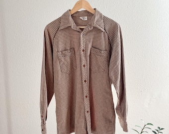 May include: A long-sleeved plaid shirt with a button-down collar and two chest pockets. The shirt is brown and tan with a small white check pattern.