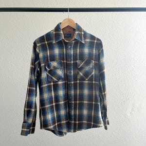 May include: A long-sleeved plaid flannel shirt in brown, blue, and white. The shirt has a button-down collar and two chest pockets.