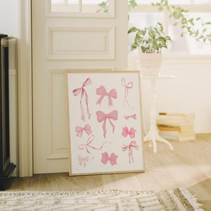 May include: A printable art print featuring a collection of pink watercolour bows in various shapes and sizes. The bows are arranged in a symmetrical pattern on a white background.