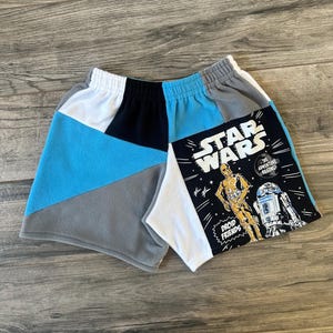 May include: Patchwork fleece shorts in blue, gray, black, and white. One leg features a Star Wars graphic with C-3PO and R2-D2, and the text "STAR WARS" and "DROID FRIENDS".