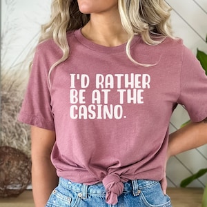 May include: A mauve t-shirt with the text "I'd rather be at the casino." printed in white.