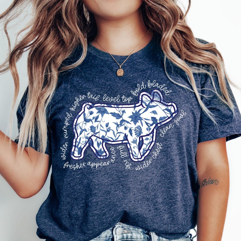 May include: A navy blue t-shirt featuring a pig illustration filled with a blue floral pattern. The pig design is outlined with text that reads "widen rumped higher tail level top bold bladed fresher appear full rib wider chest clean jowl".