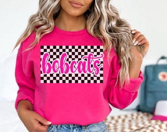 May include: Pink sweatshirt with a black and white checkered design and the word "bobcats" in pink lettering.