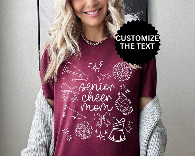 May include: Burgundy t-shirt with white graphic elements and the text "senior cheer mom." The design includes a megaphone, bows, stars, pom-poms, and a cheerleader uniform. The text "Customize the Text" is also visible.