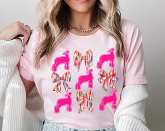 May include: Pink t-shirt with a graphic design of pink lambs and colorful bows.