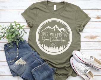 Puede incluir: Una camiseta verde con un gráfico circular blanco que presenta una cordillera, árboles y el texto "JONES FAMILY VACATION Your Destination 2023".