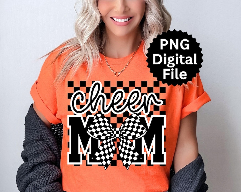 Puede incluir: Camiseta naranja con las palabras "cheer MOM" en fuente blanca y letras en bloque. Un lazo a cuadros blanco y negro est&aacute; centrado entre las palabras. Un gr&aacute;fico de estrella negra con el texto "PNG Digital File" est&aacute; en la esquina superior derecha.
