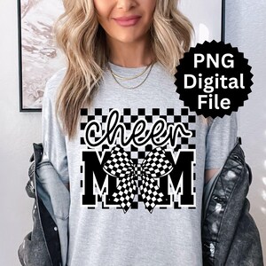 Puede incluir: Camiseta gris claro con las palabras "cheer MOM" en un dise&ntilde;o a cuadros blanco y negro. La palabra "cheer" est&aacute; en una fuente cursiva, y el lazo y la palabra "MOM" est&aacute;n en una fuente de bloque.