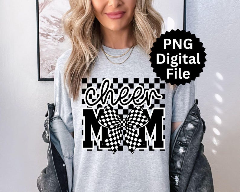Puede incluir: Camiseta gris claro con las palabras "cheer MOM" en un dise&ntilde;o a cuadros blanco y negro. La palabra "cheer" est&aacute; en una fuente cursiva, y el lazo y la palabra "MOM" est&aacute;n en una fuente de bloque.