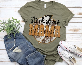 May include: A green t-shirt with a brown and white cowhide pattern lightning bolt graphic and the text "stock show MAMA" in brown letters.