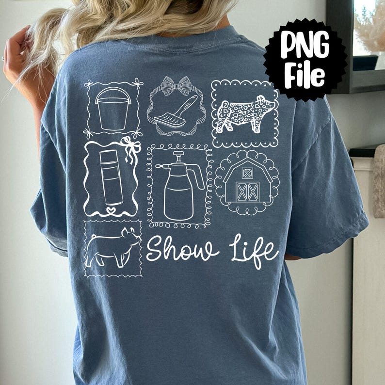 May include: A blue t-shirt with white line drawings of farm-related items, including a bucket, brush, pig, spray bottle, and barn. The words "Show Life" are written in script below the drawings. A black and white "PNG File" graphic is in the upper right corner.