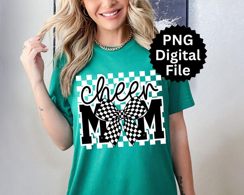 Puede incluir: Camiseta verde azulado con un gr&aacute;fico que dice "cheer MOM" en blanco y negro. El dise&ntilde;o incluye un lazo a cuadros y un fondo cuadrado a cuadros. Un logotipo de archivo digital PNG negro est&aacute; en la esquina superior derecha.