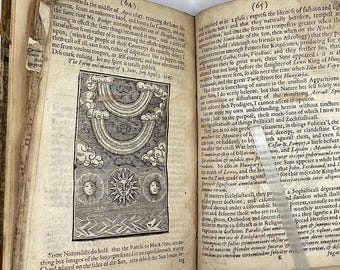 May include: Open book with aged pages, featuring a detailed black and white illustration of the sun, clouds, and celestial elements. Text in old English script surrounds the image, suggesting a historical or scientific theme. The book's cover is visible.