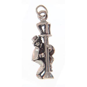 May include: Silver charm of a man in a top hat climbing a lamp post. The charm is detailed and has a vintage look.