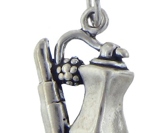 May include: A silver-toned charm featuring a lipstick, a spray can, and a cluster of grapes. The charm has a loop at the top for attachment to a necklace or bracelet. The design is detailed and three-dimensional.