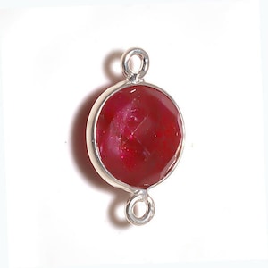 May include: A round, red gemstone pendant with a silver bail. The gemstone is set in a silver bezel and has a faceted surface.