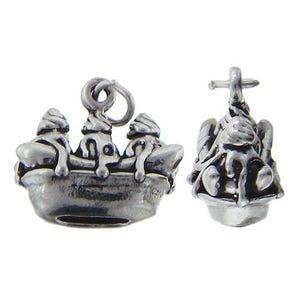May include: Two silver-toned charms. One charm depicts a boat with three figures, and the other charm is a detailed, abstract design. Both charms have a loop for attaching to a necklace or bracelet. The charms are made of a shiny metal.