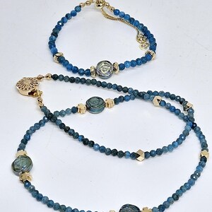 May include: A bracelet and a necklace, both featuring small, blue beads and gold-coloured accents. The necklace also includes iridescent blue-green charms. The bracelet has a delicate chain, while the necklace has decorative clasps.