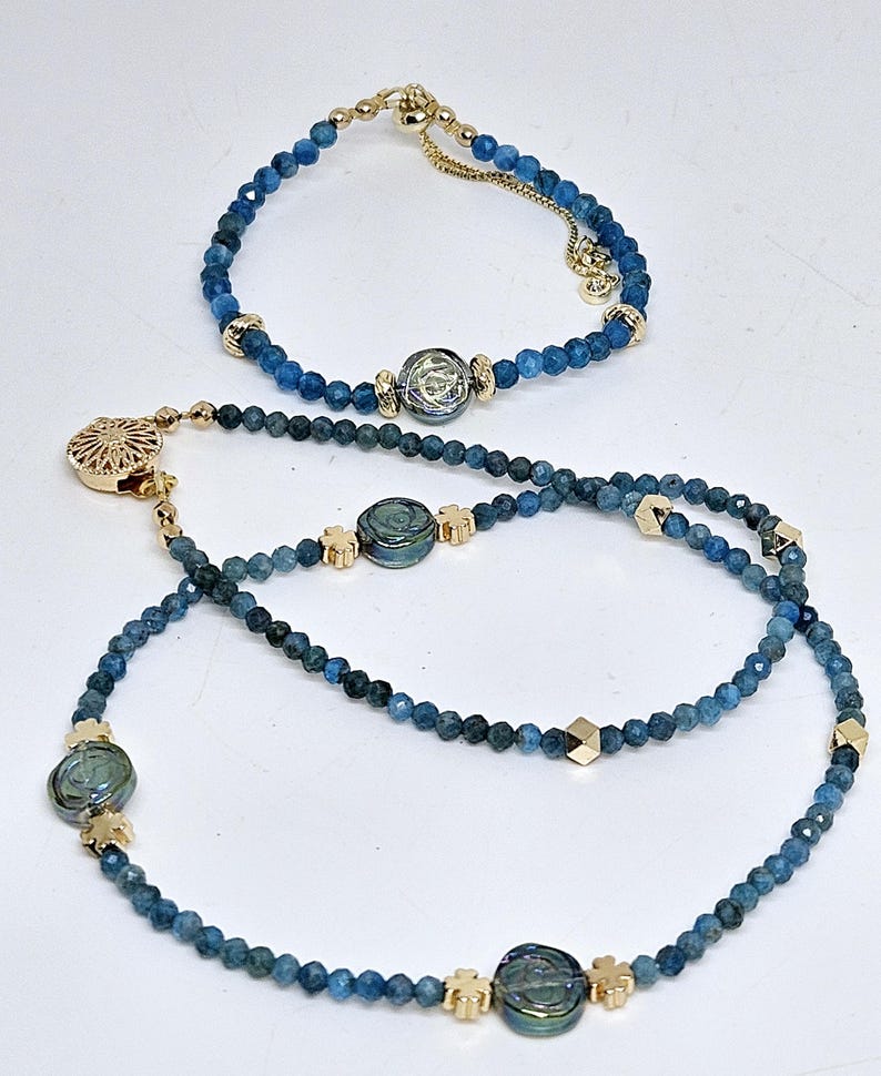 May include: A bracelet and a necklace, both featuring small, blue beads and gold-coloured accents. The necklace also includes iridescent blue-green charms. The bracelet has a delicate chain, while the necklace has decorative clasps.