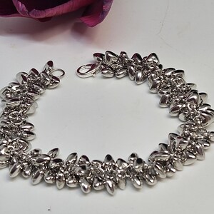 May include: A silver bracelet with a unique design featuring a series of small, pointed, leaf-like shapes.