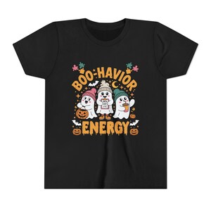 May include: Black t-shirt featuring a Halloween-themed graphic. The design includes three cartoon ghosts wearing hats and holding a pumpkin, a clipboard, and a coffee cup. The text reads "Boo-havior Energy."