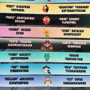 May include: Eight horizontal fabric lanyards in various pastel and solid colors, each featuring two names printed in black text and a small central cartoon character icon. The names include Boom, Tharatorn, Aou, First, Force, Joong, Dunk, Perth, Santa, Pond, Phuwin, Tay, New, William, and Est.