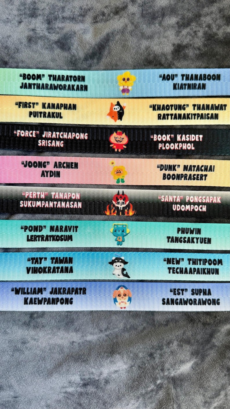 May include: Eight horizontal fabric lanyards in various pastel and solid colors, each featuring two names printed in black text and a small central cartoon character icon. The names include Boom, Tharatorn, Aou, First, Force, Joong, Dunk, Perth, Santa, Pond, Phuwin, Tay, New, William, and Est.