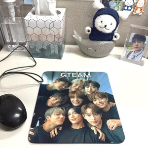 May include: A black and white mousepad with a group of young men smiling and posing for a photo. The mousepad has the text "&TEAM" printed on it.
