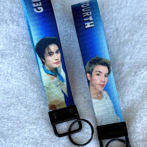 May include: Two blue fabric keychains featuring printed portraits of individuals. One strap displays the text GEMINI and the other displays FOURTH. Each keychain includes a black metal clasp and a circular black metal key ring attached at the base.
