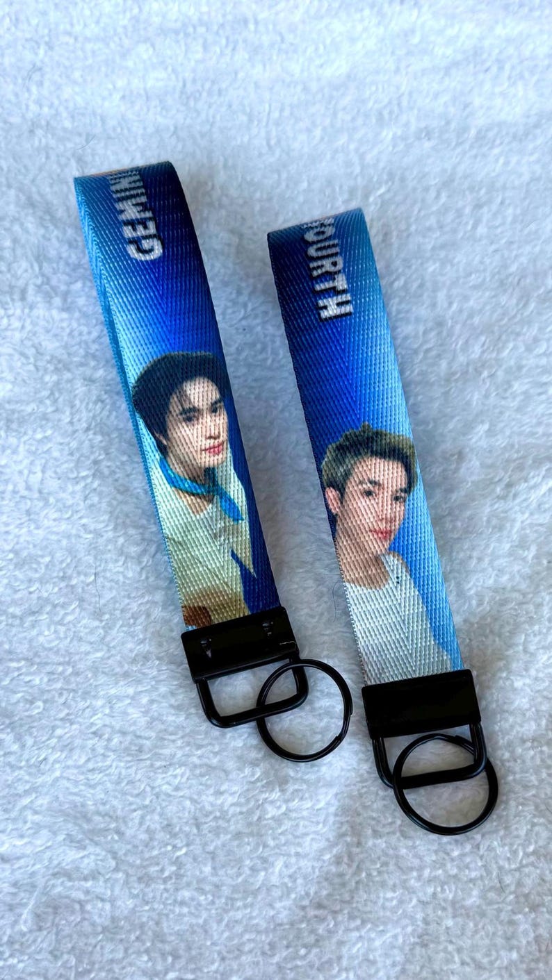 May include: Two blue fabric keychains featuring printed portraits of individuals. One strap displays the text GEMINI and the other displays FOURTH. Each keychain includes a black metal clasp and a circular black metal key ring attached at the base.