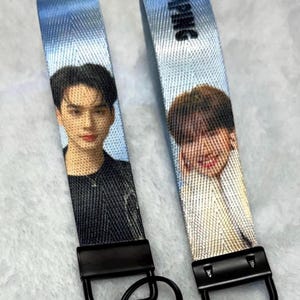 May include: Two light blue fabric keychains featuring printed portraits of individuals. Each strap has a black metal clasp and a circular black keyring. The right strap displays the text JUMPING in black letters at the top, while the left strap shows a person in a black shirt.