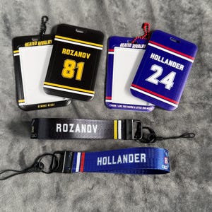 May include: A collection of ID badge holders and wrist lanyards. The badge holders are black and blue with white text and yellow accents. The wrist lanyards are black and blue with white text. The text includes the names "ROZANOV" and "HOLLANDER" and numbers.