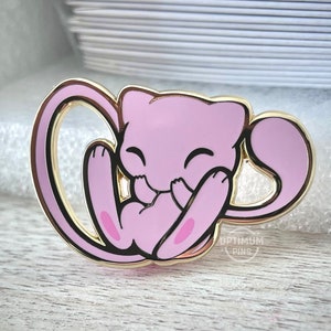 Puede incluir: Un pin de esmalte dorado y rosa con un personaje de dibujos animados rosa de Pokemon con una cola enroscada. El personaje sonríe y sostiene su cola con sus patas. El pin está hecho por Optimum Pins.