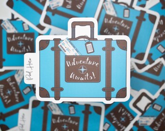 May include: A light blue suitcase sticker with brown accents, a handle, and a luggage tag. The sticker has the words "Adventure Awaits!" in a brown rectangle with a compass design. A boarding pass is in the pocket.