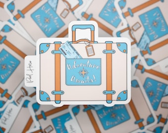 May include: A sticker featuring a cream-colored suitcase with orange and blue accents. The suitcase has a blue pocket with the words "Adventure Awaits!" and a compass design. A boarding pass and luggage tag are also visible.