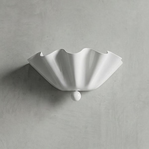 Könnte beinhalten: Eine weiße, an der Wand befestigte dekorative Schale mit gewelltem Rand. Die Schale hat einen abgerundeten Boden und einen kleinen, kugelförmigen Akzent. Das Design ist minimalistisch und modern, geeignet für die Inneneinrichtung.