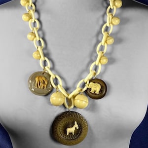 May include: A white plastic necklace with large round beads and four charms. The charms are made of brown and white plastic and feature animal figures. The necklace is on a mannequin.