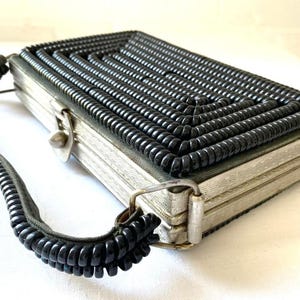 Op de afbeelding: Een vintage zwarte en zilveren handtas met een uniek ontwerp. De tas is gemaakt van gekruld zwart koord en heeft een zilveren sluiting. De tas heeft een zwarte koordschouderband.