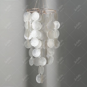 May include: A white shell chandelier with a gold metal frame. The shells are arranged in a cascading pattern, creating a unique and elegant design.